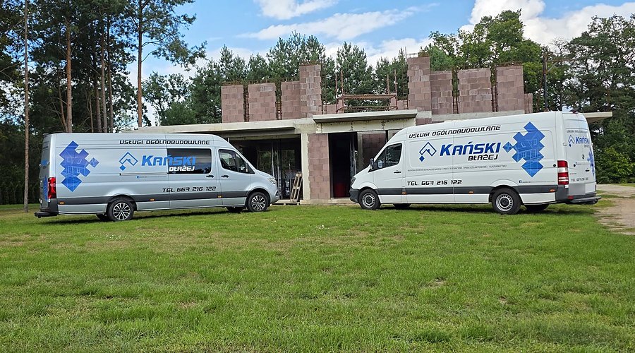 Dwa firmowe busy z&nbsp;logo Kański przed budynkiem w&nbsp;stanie surowym